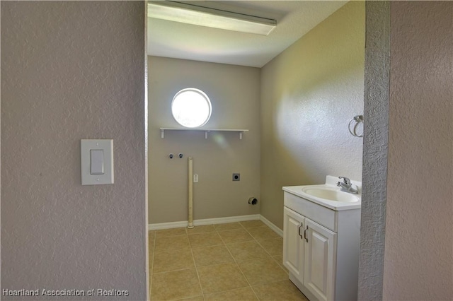 laundry area featuring electric dryer hookup, a sink, cabinet space, light tile patterned floors, and a textured wall