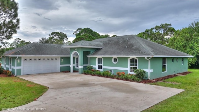 single story home with a shingled roof, concrete driveway, a front yard, stucco siding, and a garage