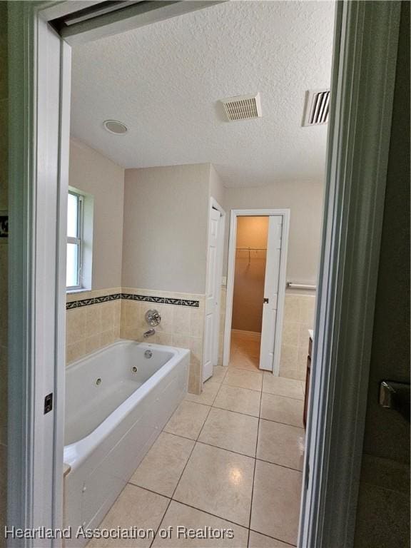 full bath with visible vents, tile walls, tile patterned floors, a tub with jets, and a textured ceiling