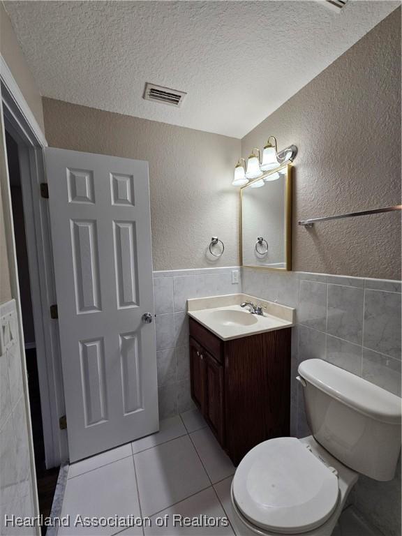 half bathroom with visible vents, a textured ceiling, tile walls, vanity, and a textured wall