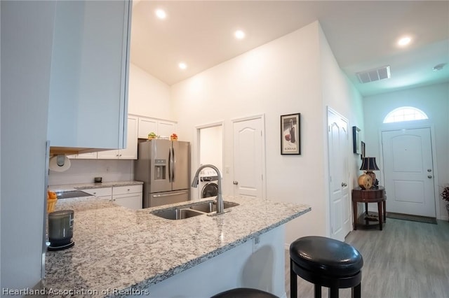 kitchen with sink, light stone counters, stainless steel fridge, vaulted ceiling, and white cabinets