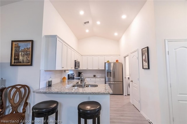 kitchen featuring kitchen peninsula, light stone counters, stainless steel appliances, sink, and white cabinetry