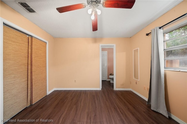 unfurnished bedroom with ensuite bath, ceiling fan, a closet, and dark wood-type flooring