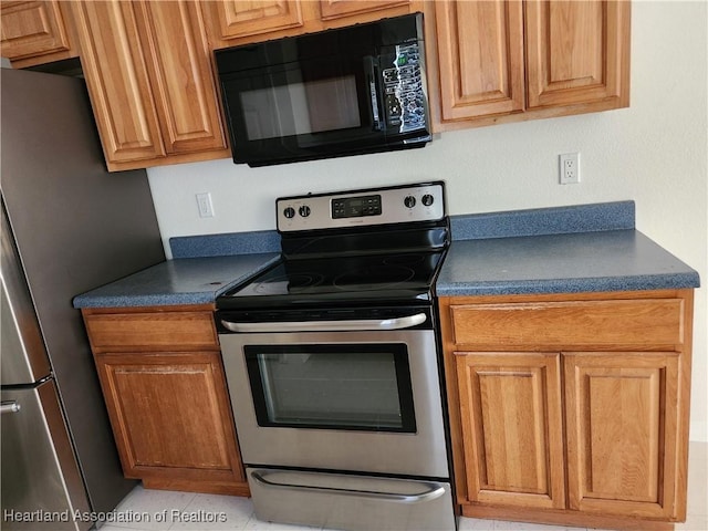 kitchen featuring brown cabinetry, stainless steel appliances, and dark countertops