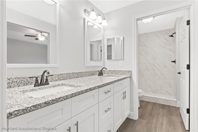 bathroom featuring vanity, ceiling fan, toilet, a tile shower, and wood-type flooring