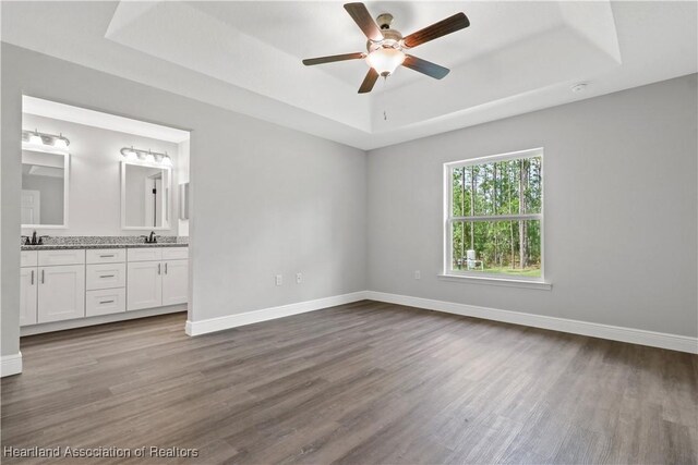 unfurnished bedroom with ensuite bathroom, ceiling fan, a raised ceiling, and sink