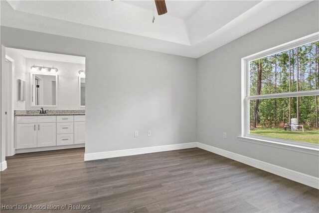 unfurnished bedroom featuring connected bathroom, ceiling fan, dark wood-type flooring, and multiple windows