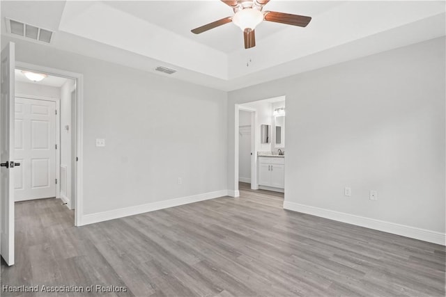 unfurnished room with ceiling fan, sink, a tray ceiling, and light hardwood / wood-style flooring