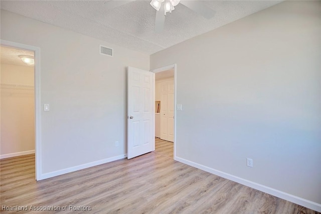 unfurnished bedroom featuring light wood-type flooring, a walk in closet, a textured ceiling, ceiling fan, and a closet