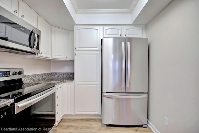 kitchen featuring dark stone countertops, light wood-type flooring, ornamental molding, appliances with stainless steel finishes, and white cabinetry