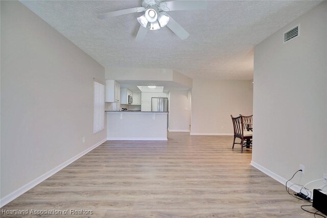 unfurnished living room with ceiling fan, light hardwood / wood-style flooring, and a textured ceiling