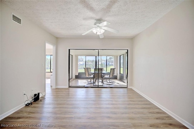 empty room with ceiling fan, light wood-type flooring, and a textured ceiling