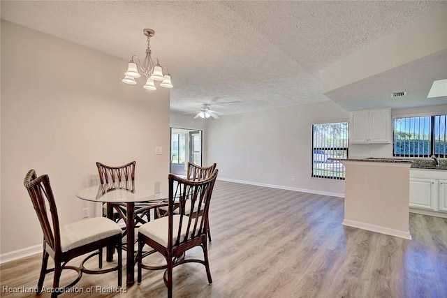 dining room with ceiling fan with notable chandelier, sink, light wood-type flooring, and a textured ceiling