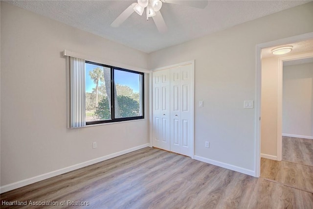 unfurnished bedroom with a textured ceiling, light wood-type flooring, a closet, and ceiling fan