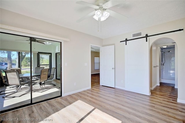 spare room with ceiling fan, a barn door, and light hardwood / wood-style flooring