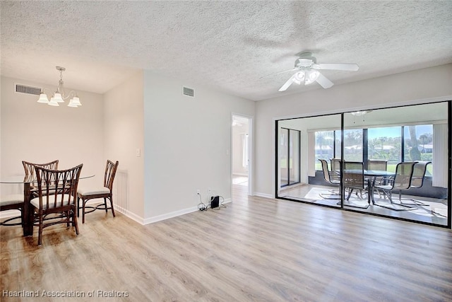 dining room with ceiling fan with notable chandelier, light wood-type flooring, and a textured ceiling