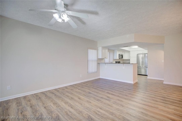 unfurnished living room with a textured ceiling, light hardwood / wood-style flooring, and ceiling fan