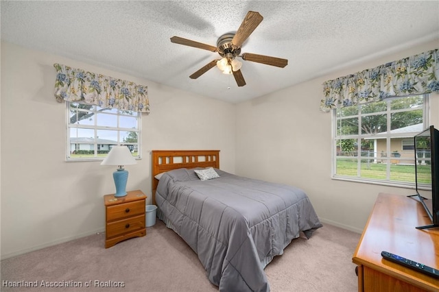 bedroom with ceiling fan, light colored carpet, and a textured ceiling