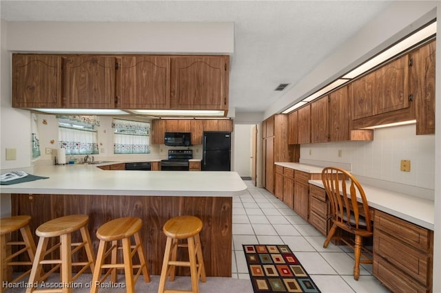 kitchen featuring kitchen peninsula, light tile patterned floors, a breakfast bar area, and black appliances