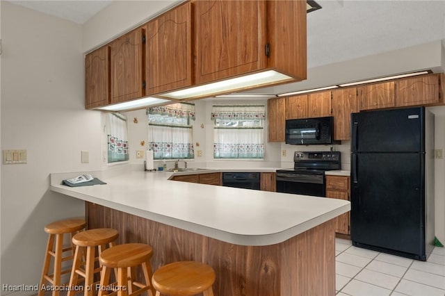 kitchen with sink, kitchen peninsula, a breakfast bar area, light tile patterned floors, and black appliances