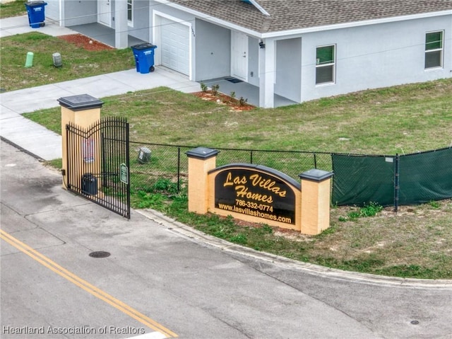 community / neighborhood sign featuring an attached garage, a gate, fence, and a yard