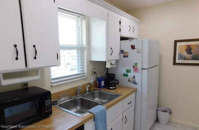 kitchen with black microwave, a sink, white cabinetry, light countertops, and freestanding refrigerator