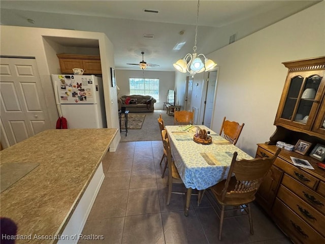 dining room featuring ceiling fan with notable chandelier, dark tile patterned floors, and lofted ceiling