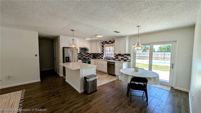 kitchen featuring appliances with stainless steel finishes, tasteful backsplash, pendant lighting, white cabinets, and a center island