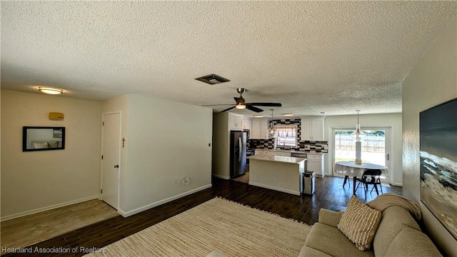 kitchen with stainless steel fridge, dark hardwood / wood-style flooring, a kitchen island, white cabinetry, and hanging light fixtures