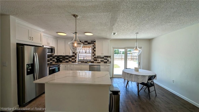 kitchen featuring white cabinets, backsplash, decorative light fixtures, a kitchen island, and appliances with stainless steel finishes