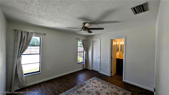 unfurnished bedroom with a textured ceiling, dark hardwood / wood-style flooring, ensuite bathroom, and ceiling fan