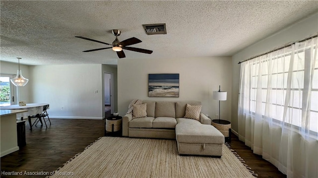 living room with a textured ceiling, ceiling fan, and dark wood-type flooring