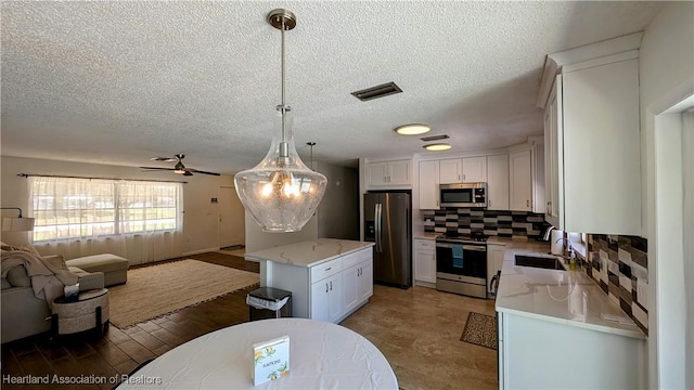 kitchen with hanging light fixtures, tasteful backsplash, white cabinets, a kitchen island, and appliances with stainless steel finishes