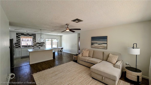 living room featuring ceiling fan, sink, dark wood-type flooring, and a textured ceiling