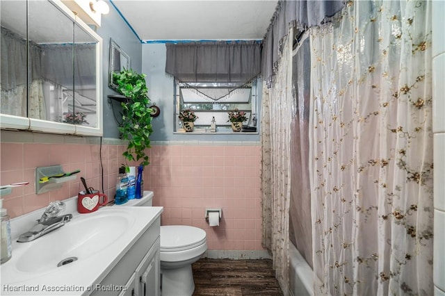 full bathroom with shower / bathtub combination with curtain, hardwood / wood-style floors, toilet, vanity, and tile walls