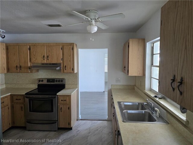 kitchen with a sink, stainless steel range with electric cooktop, light countertops, under cabinet range hood, and visible vents