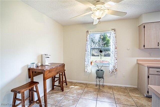 interior space with ceiling fan, light brown cabinets, a textured ceiling, and light tile patterned floors