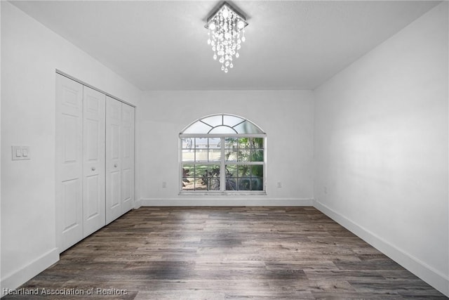 unfurnished bedroom featuring an inviting chandelier, baseboards, a closet, and wood finished floors