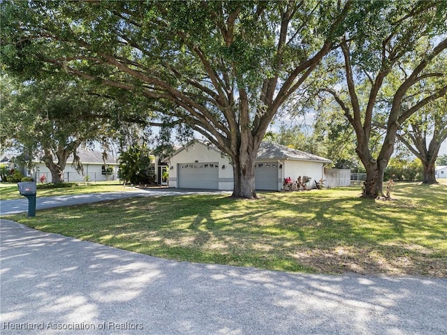 view of property hidden behind natural elements featuring stucco siding, fence, driveway, and a front lawn
