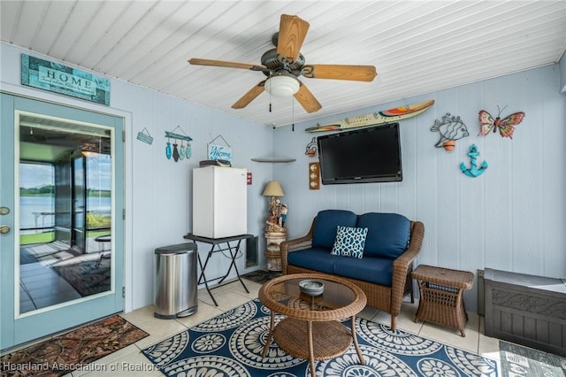 living area featuring wood walls, light tile patterned floors, and ceiling fan