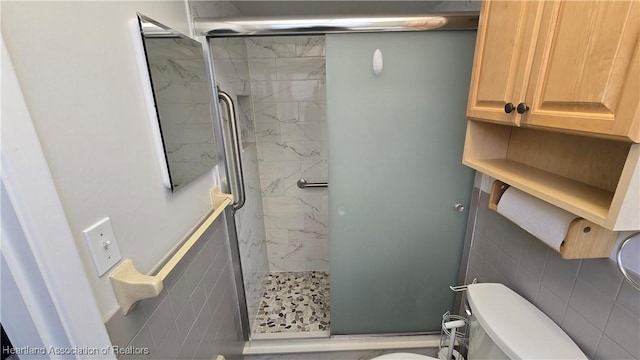 bathroom featuring a shower with door, tile walls, and toilet