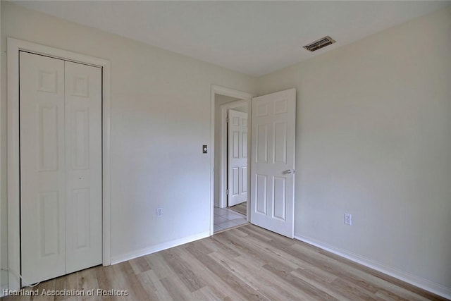 unfurnished bedroom with visible vents, baseboards, light wood-style floors, and a closet