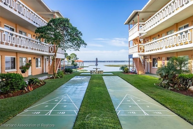 surrounding community with shuffleboard, stairway, a lawn, and a water view