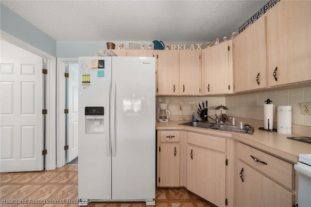 kitchen featuring light brown cabinetry, a sink, light countertops, white refrigerator with ice dispenser, and a textured ceiling