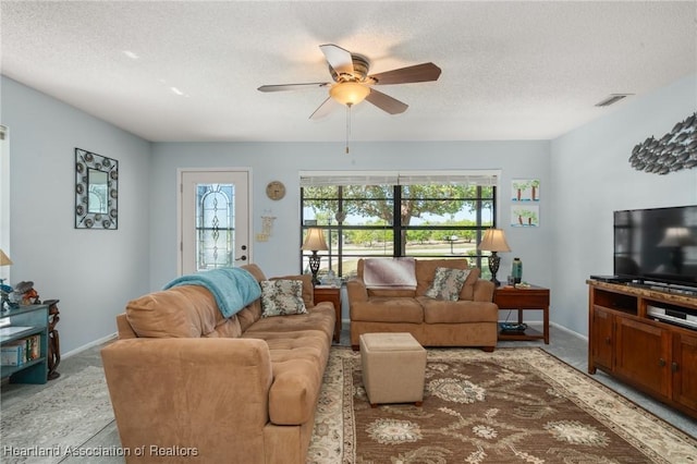 living room with baseboards, a ceiling fan, visible vents, and a textured ceiling