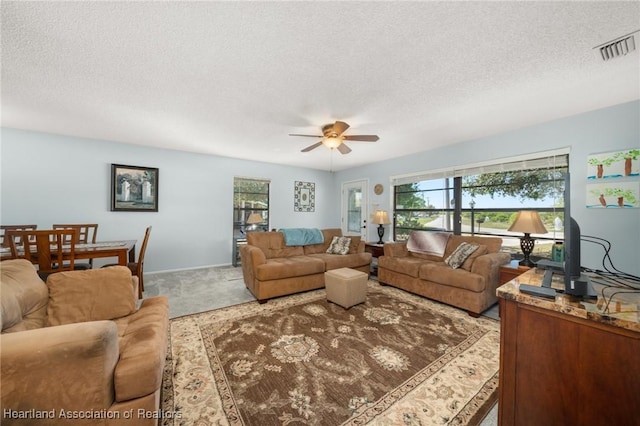 carpeted living room with a textured ceiling, visible vents, and ceiling fan