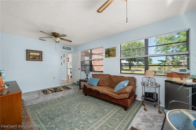 carpeted living area with baseboards, a textured ceiling, and a ceiling fan