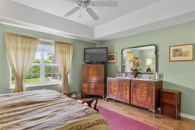 bedroom featuring ceiling fan, light wood-type flooring, and a raised ceiling