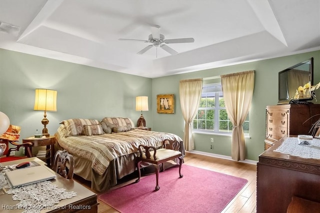 bedroom featuring ceiling fan, light hardwood / wood-style floors, and a tray ceiling