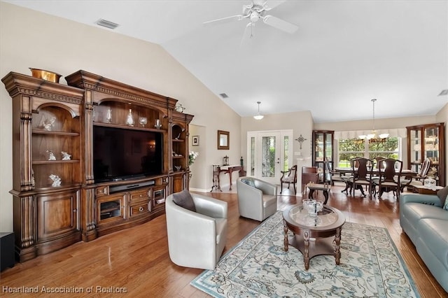 living room featuring vaulted ceiling, ceiling fan with notable chandelier, and wood-type flooring